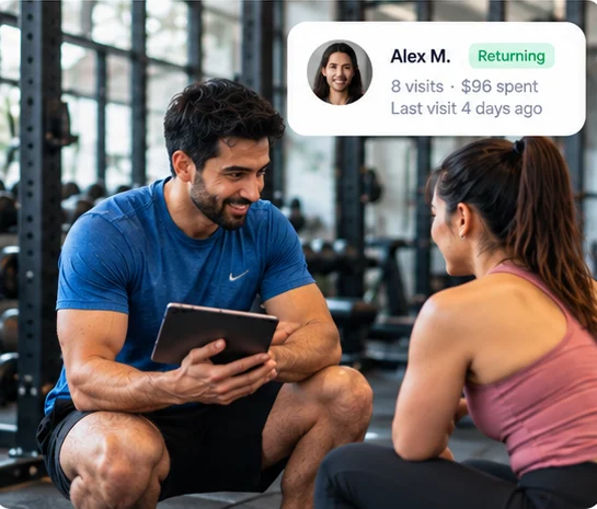 A gym trainer checks a returning customer's visit history on a tablet
